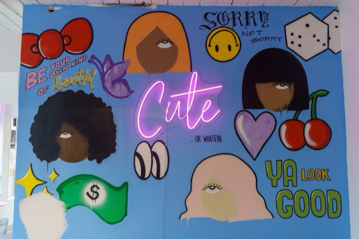 A colorful mural with a pink neon Cute sign