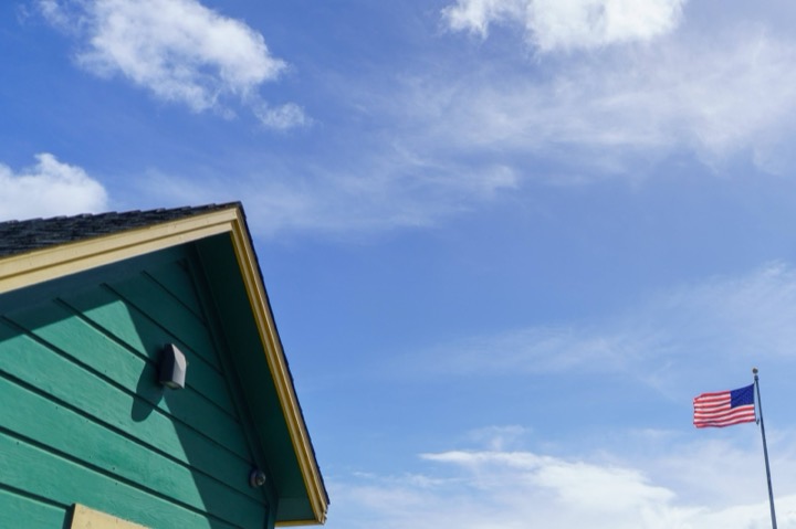 The corner of a green house with an American flag against the sky