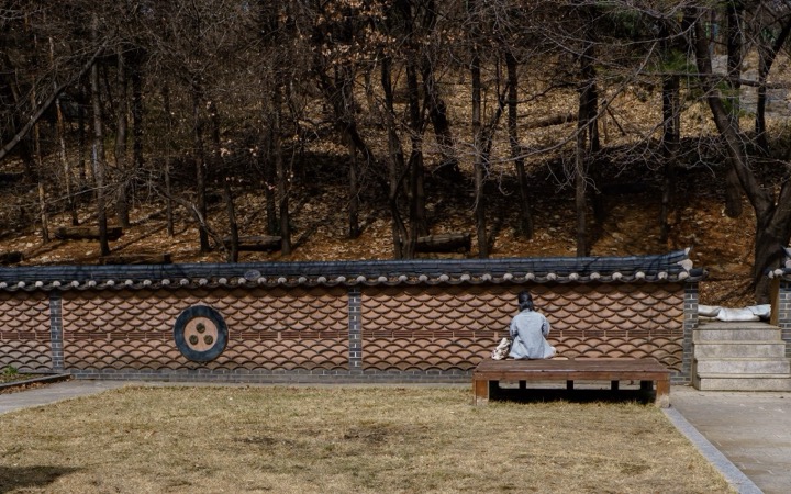 A person sitting on a bench beside a traditional tiled wall