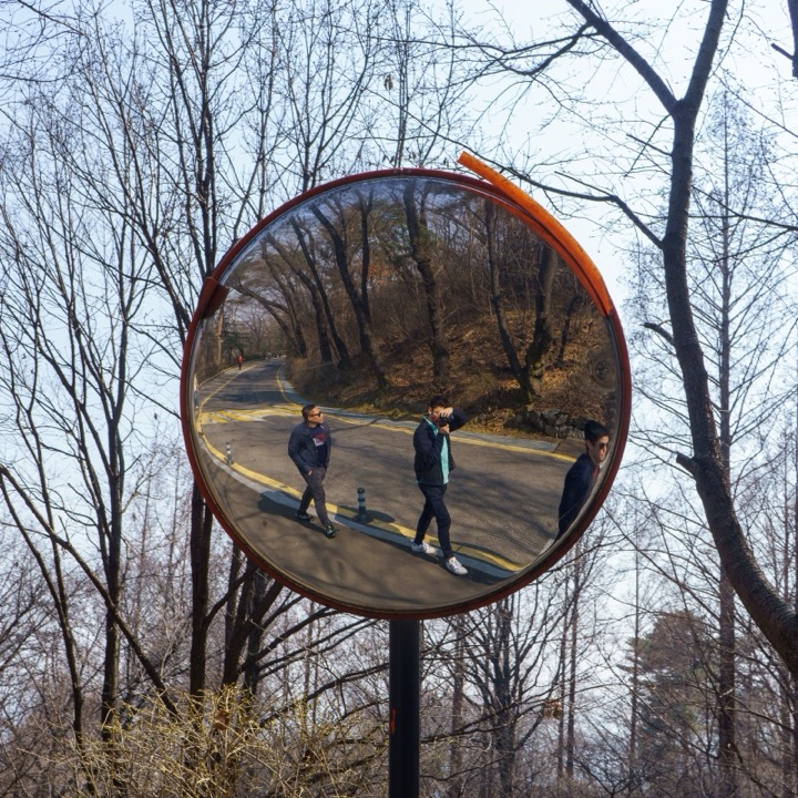 A convex road mirror reflecting people walking among bare trees