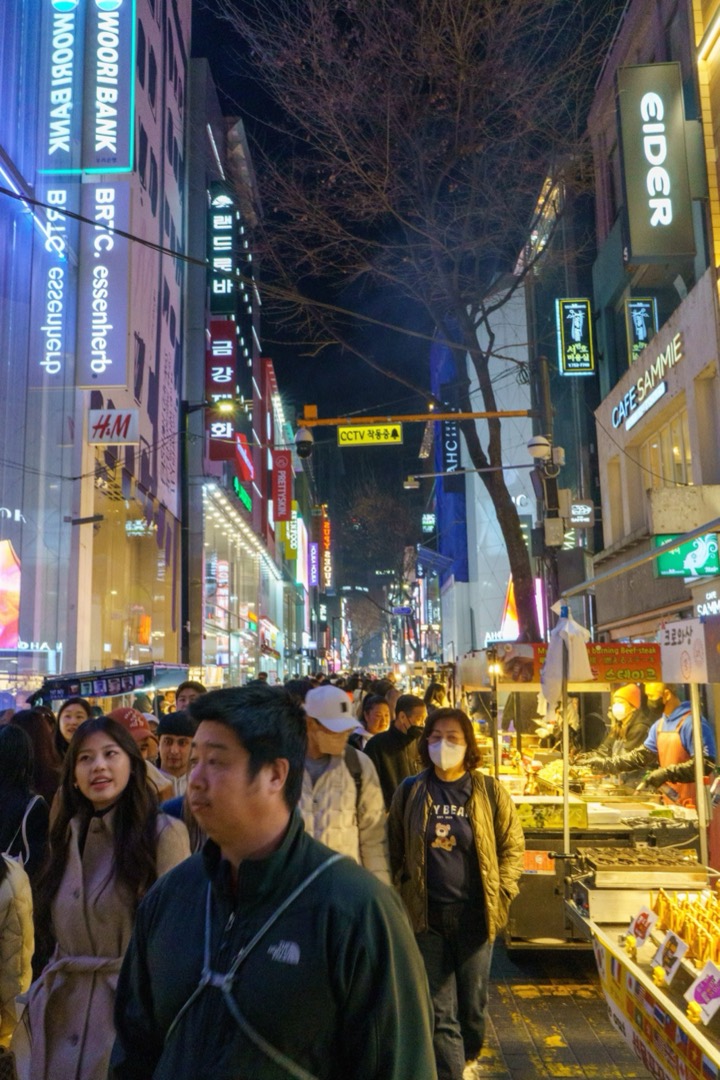 A crowded street at night, lit by neon signs