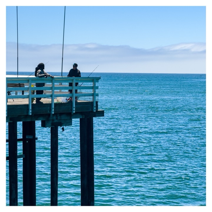 Two people fishing from a pier over turquoise water