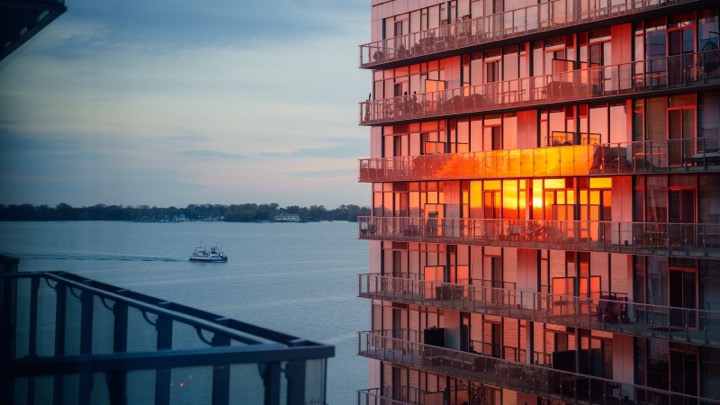 Sunset reflected in the windows of a lakeside high-rise, with a boat on the water